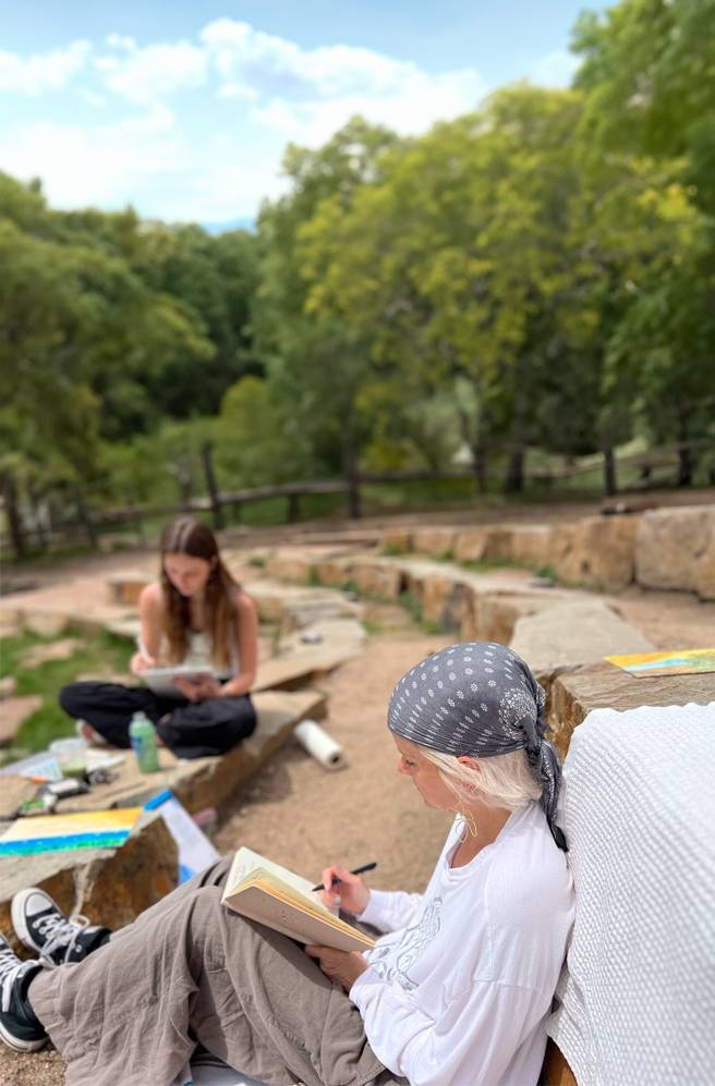 Mother and daughter writing in notebooks outside in a rocky setting